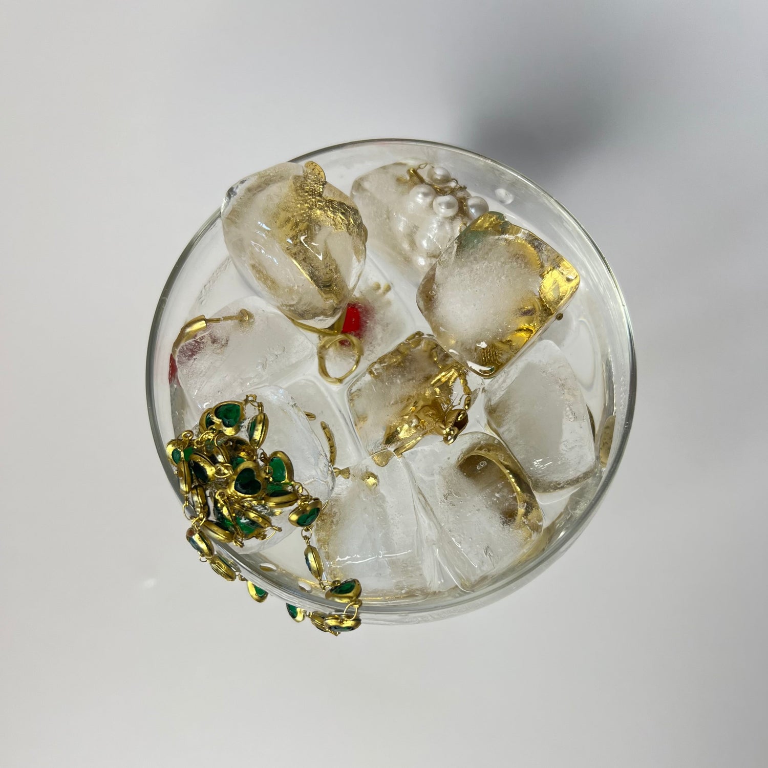Bijoux dorés Héra Jewelry — bagues, boucles d’oreilles et piercings tendance incrustés dans des glaçons, présentés dans une coupe en verre transparente, mise en scène artistique, photo élégante, bijoux femme, accessoires mode luxe, style chic et moderne.
